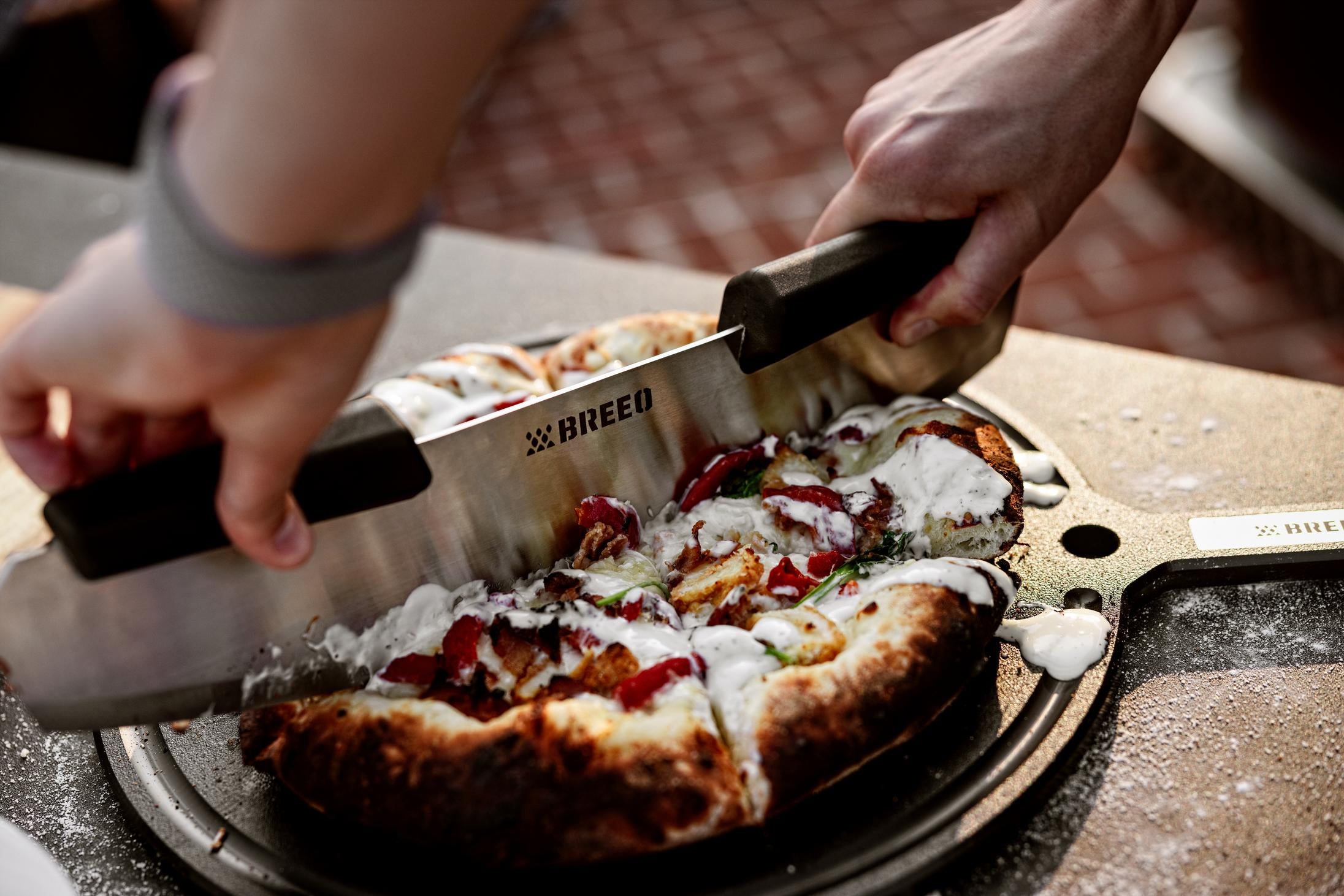 This is an image of a person using the Pizza Rocker to slice pizza on the Breeo Serving Board