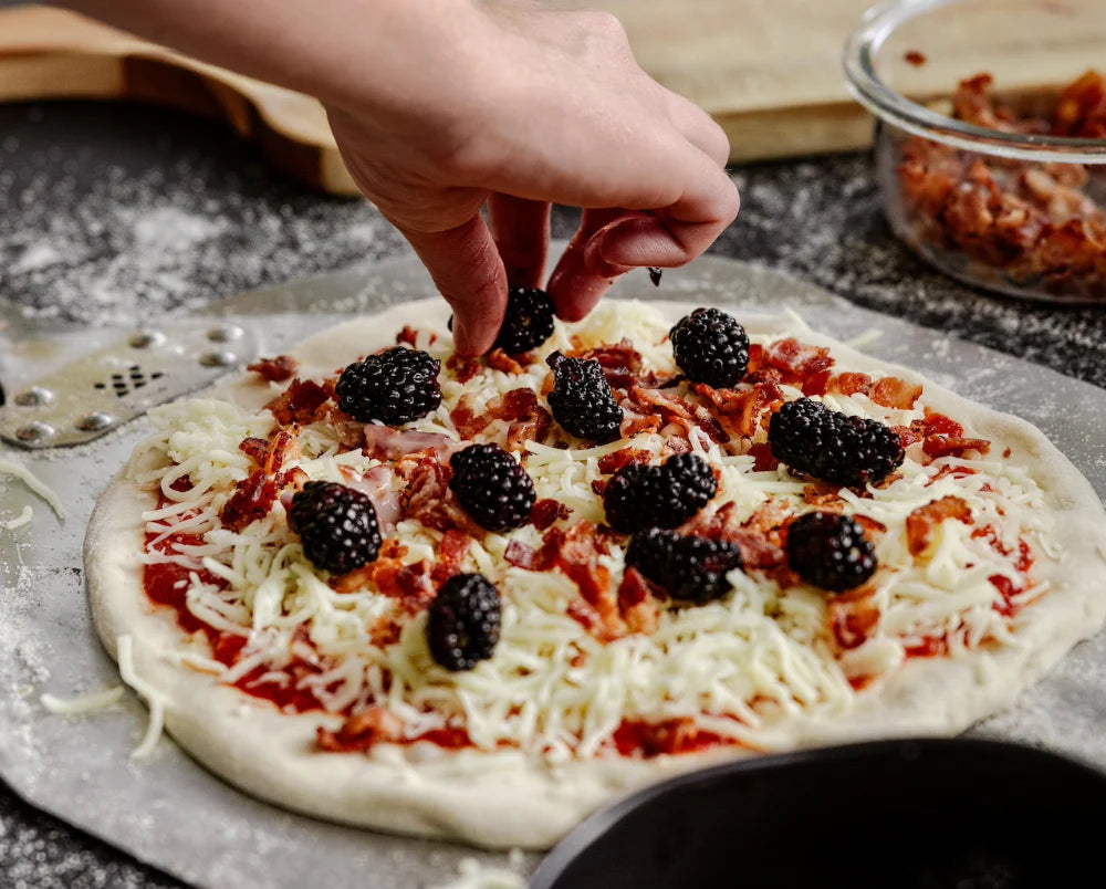 person putting toppings on pizza
