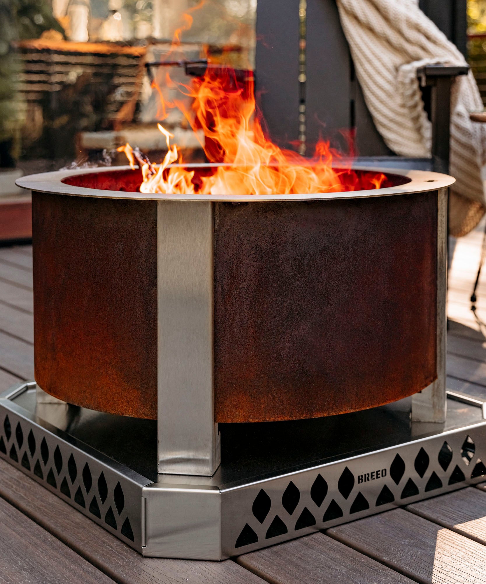 Breeo corten smokeless firepit on wood patio with breeo chair in background