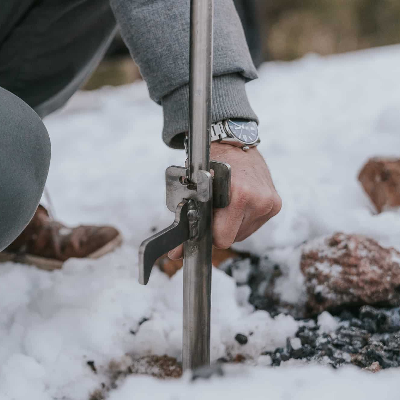 Man wearing a watch putting the Outpost Anchorpoint in snow-covered ground
