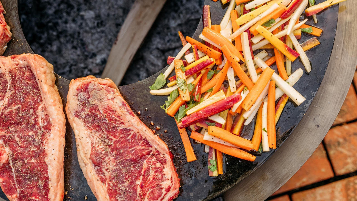 An image of steaks and vegetables searing on a Breeo SearPlate Griddle