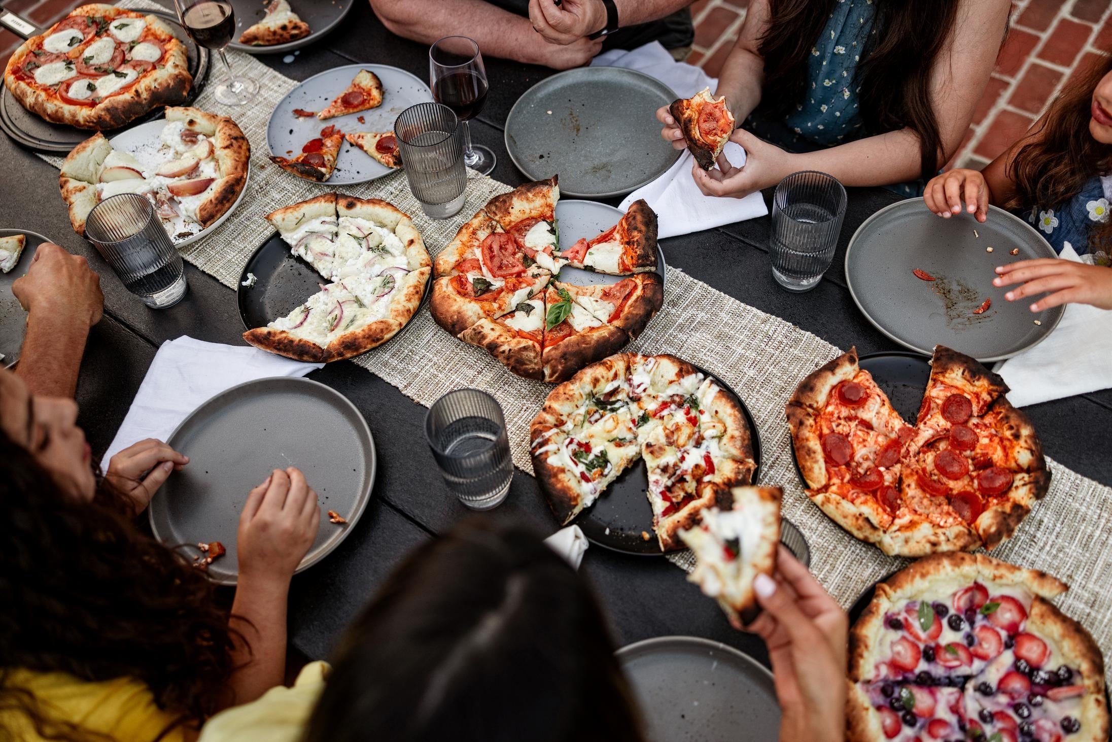 An image of Neapolitan style pizzas spread out on a table with friends gathered around enjoying it. 