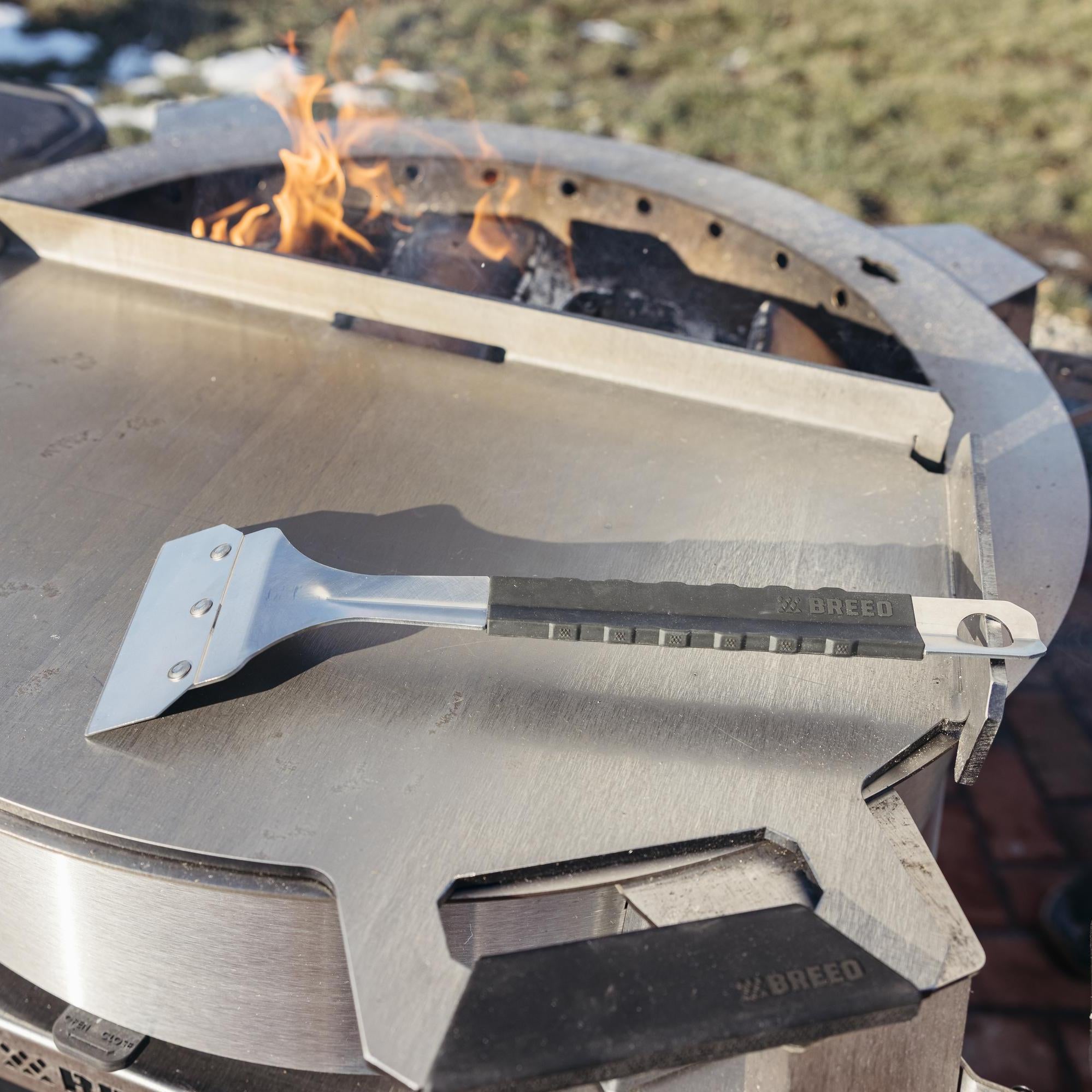 Portable grill with a breeo scraper on top, set against a natural outdoor background.