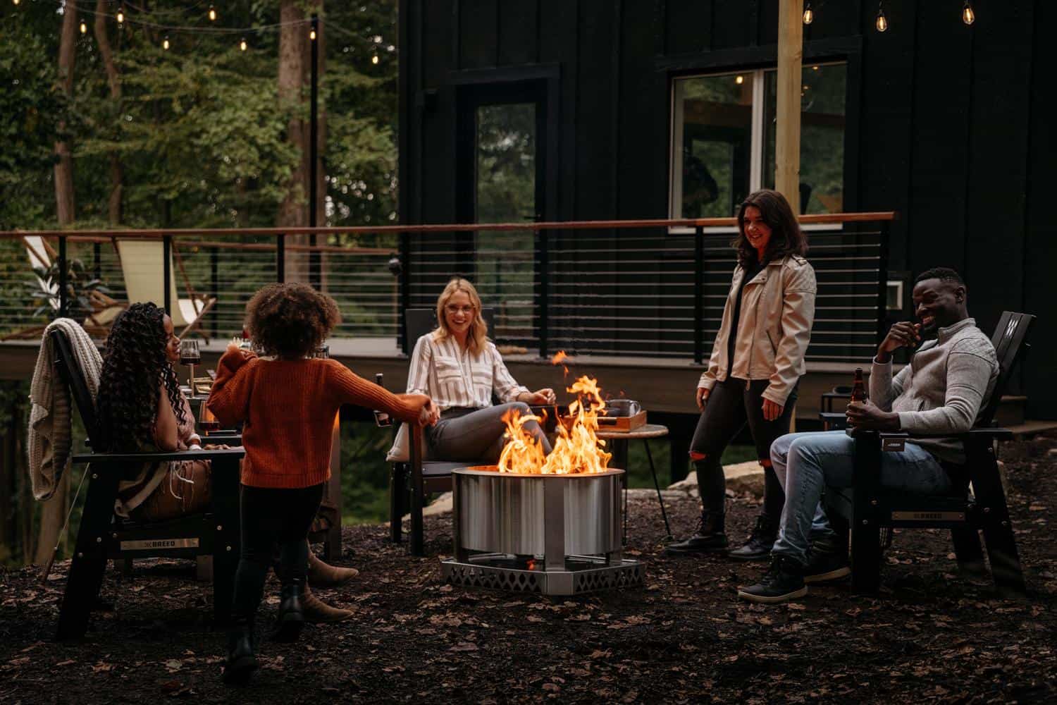 This is an image of friends gathered on Breeo chairs sitting around a Stainless X Series firepit. 