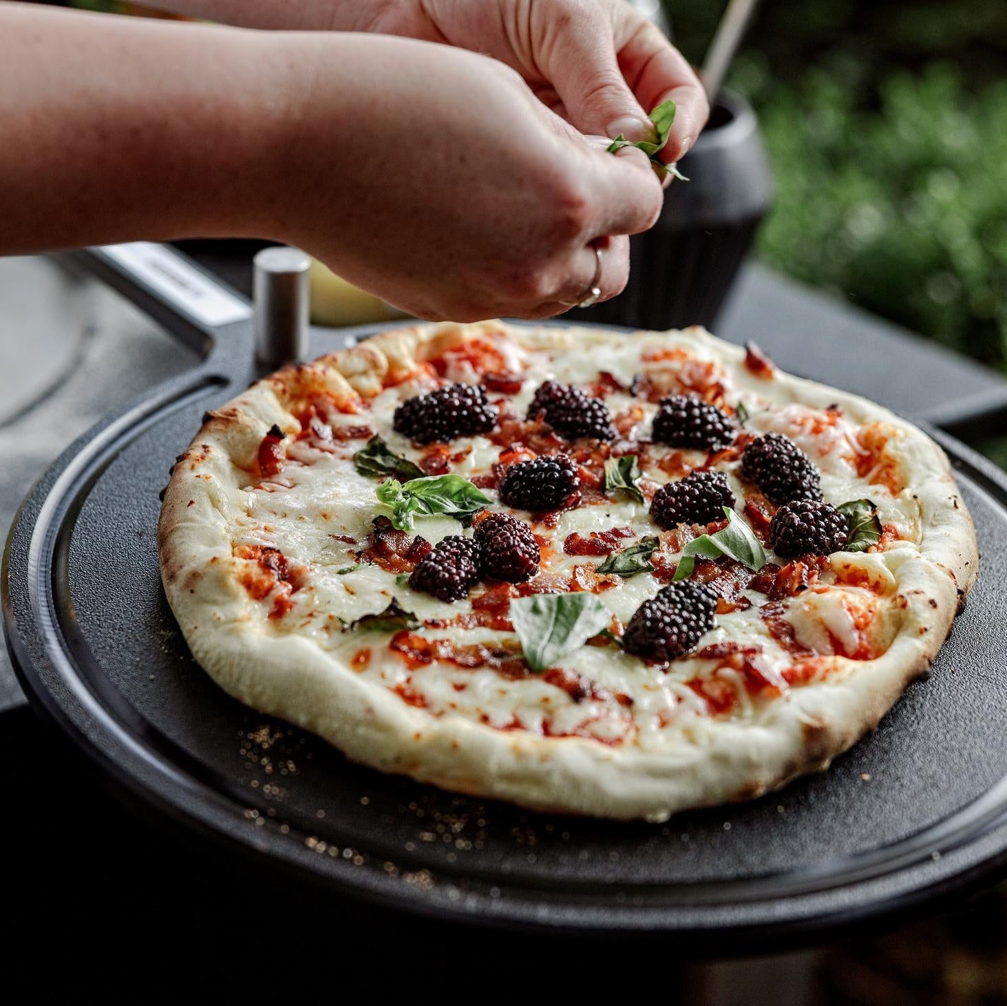 This is an image of someone sprinkling basil on a pizza resting on the Serving Board. 
