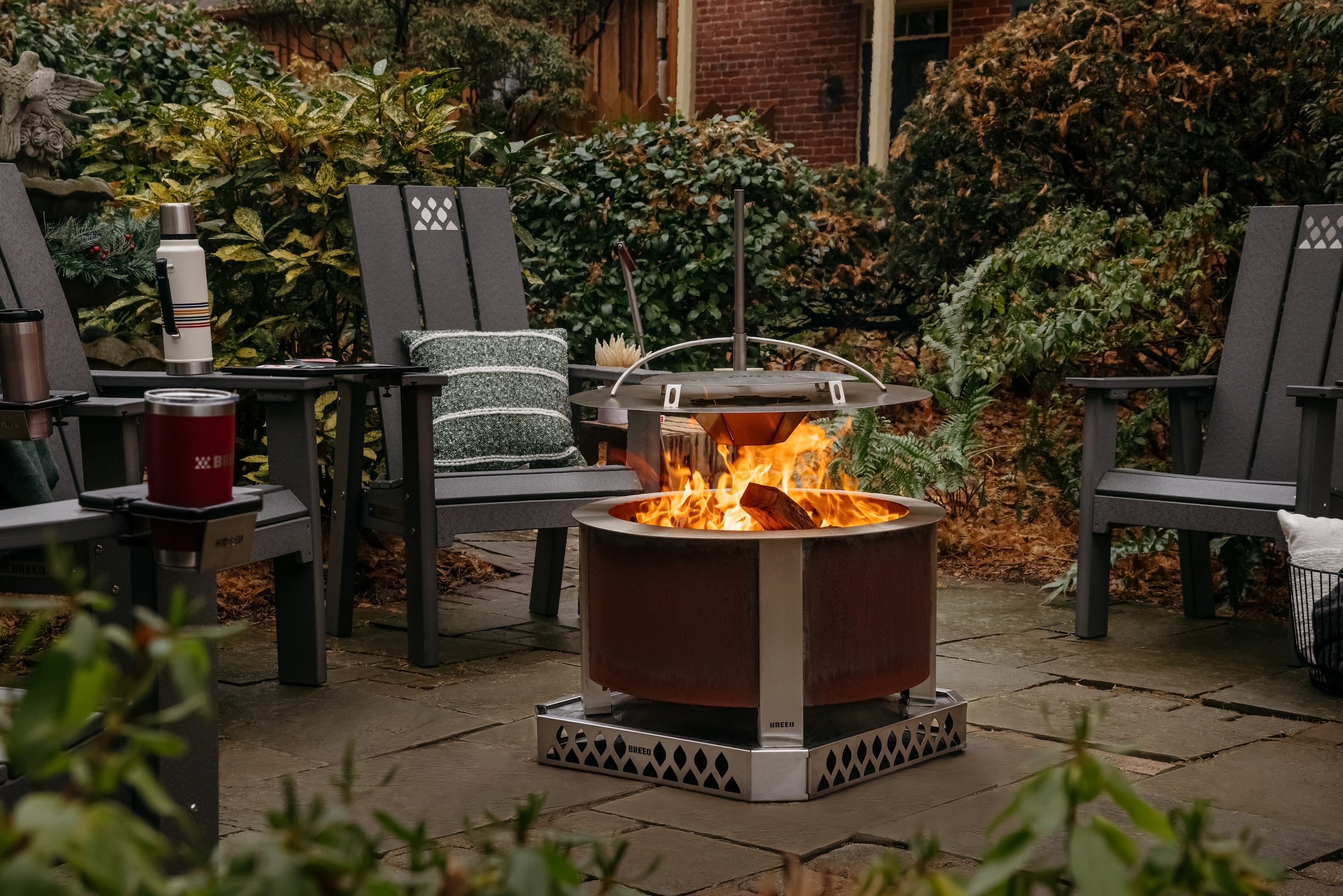 Outdoor patio scene with a x series fire pit,  x series chairs, and drinks on a stone patio.