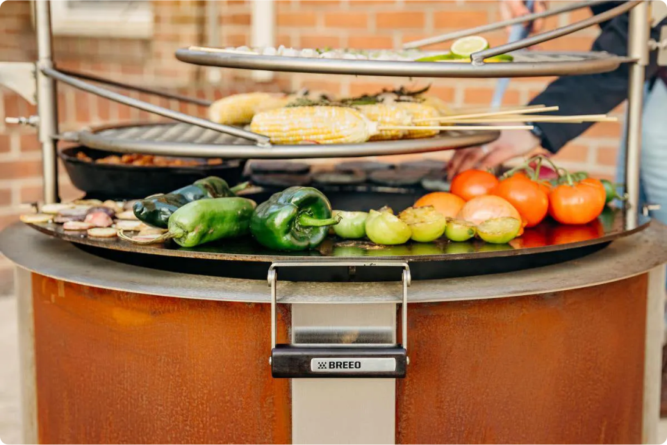 An image of the X30 Corten firepit that is used for grilling with two Outpost Grills and a Searplate Griddle attached. 