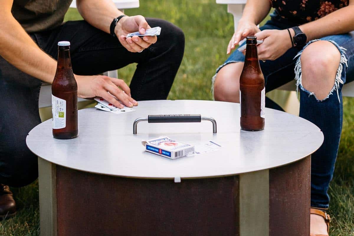 An image of two people playing cards on an X Series firepit with the lid on