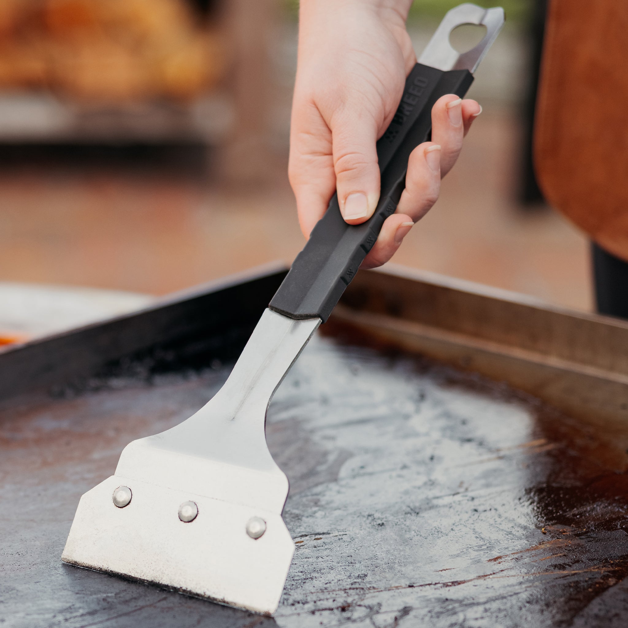 Person using a griddle scrapper on a hot grill