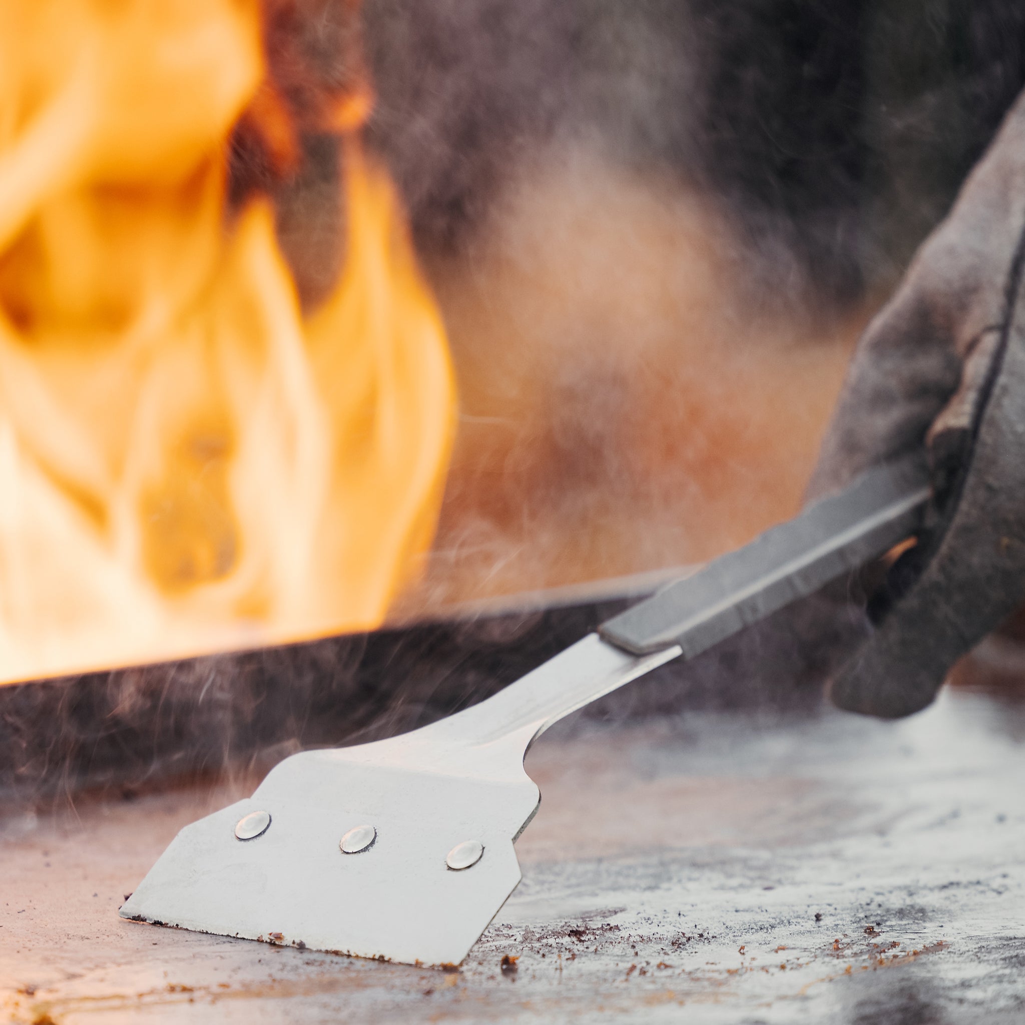 Metal spatula over a fire with flames and smoke in the background