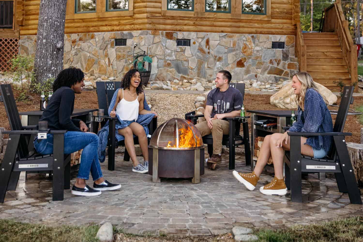 This is an image of friends sitting together around a Breeo firepit with X Series chairs and tables. 